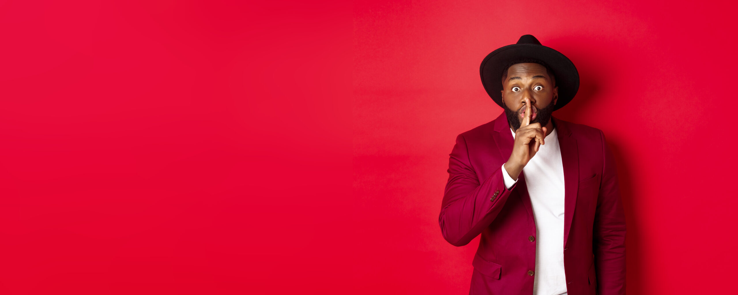 Fashion and party concept. African american man in classy hat hushing, asking keep secret, preparing surprise, standing over red background.